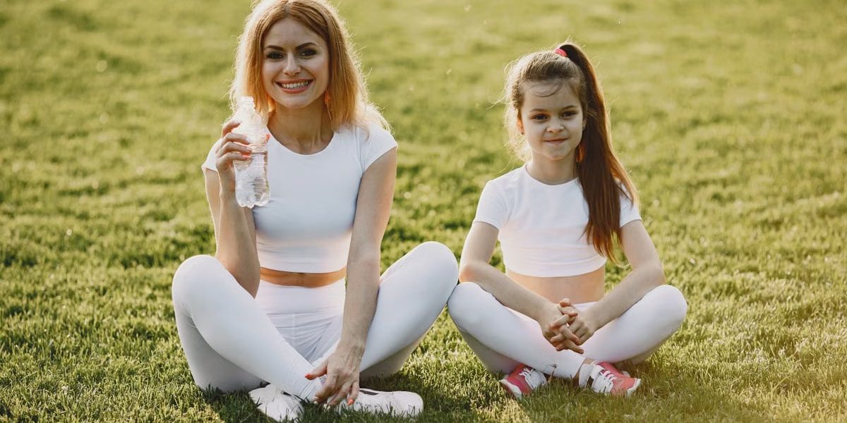 Smiling mother and daughter wearing matching outfits sitting on grass in a park.