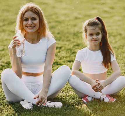Smiling mother and daughter wearing matching outfits sitting on grass in a park.