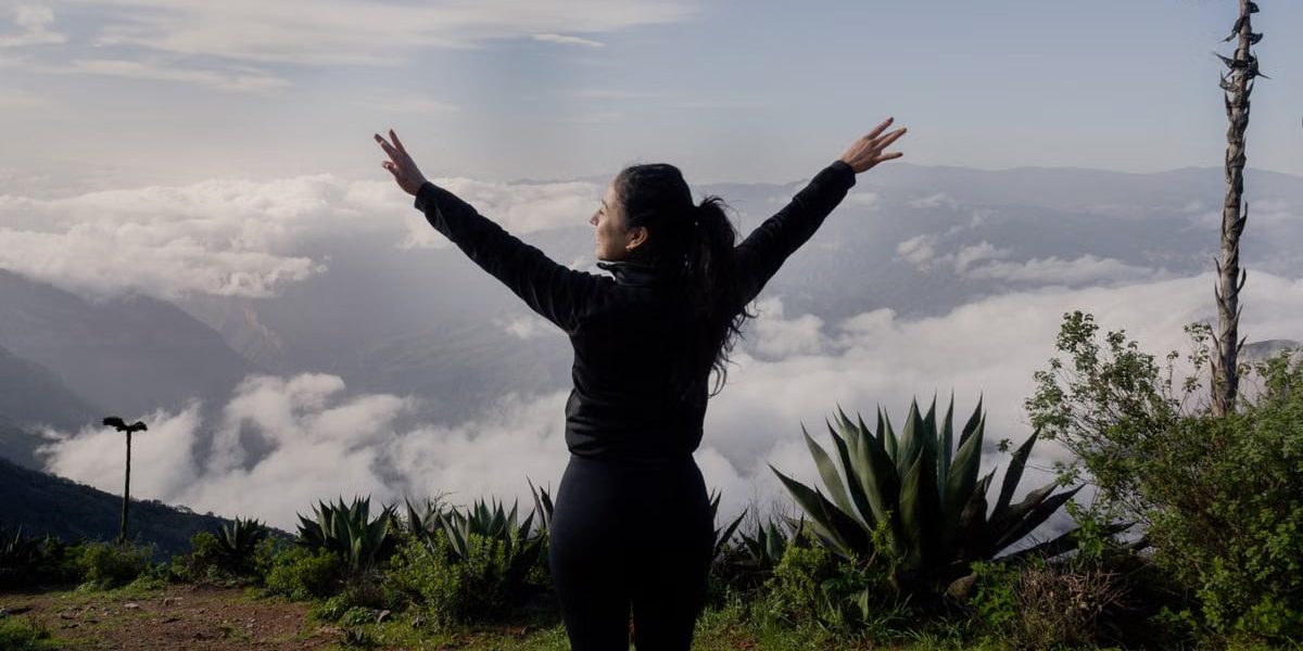 A woman with arms raised enjoying a scenic mountain view in Pinal de Amoles, Mexico.