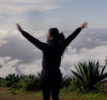 A woman with arms raised enjoying a scenic mountain view in Pinal de Amoles, Mexico.